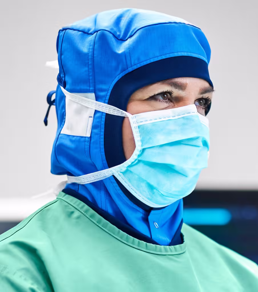 Närbild på ansiktet av en operationssjuksköterska i en operationssal med munskydd och huva.